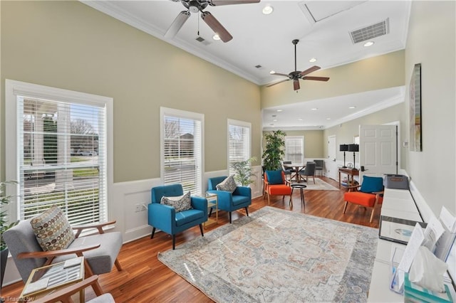 living area with visible vents, wainscoting, crown molding, and a ceiling fan