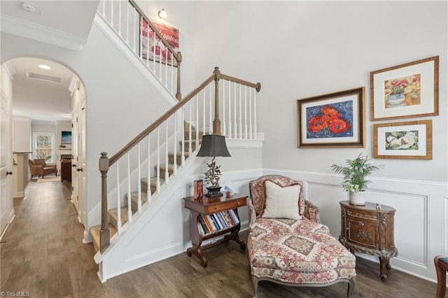 stairs with arched walkways, wood finished floors, and ornamental molding