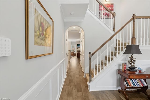 corridor with wood finished floors, arched walkways, crown molding, a decorative wall, and stairs