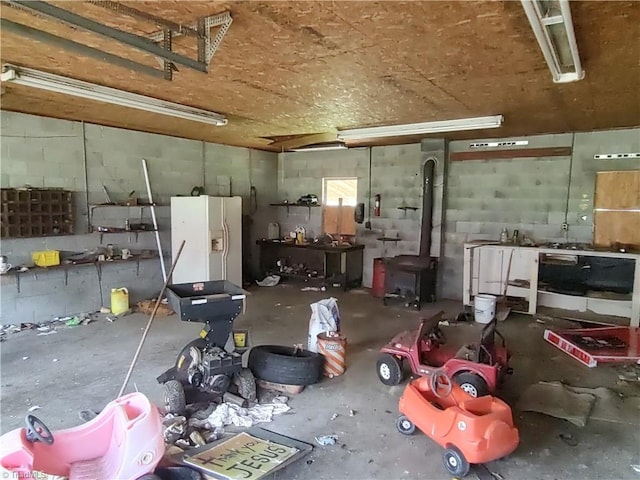 345 Anderson Rd, Eden, NC 27288 - garage with a wood stove, a workshop area, white refrigerator with ice dispenser, and concrete block wall