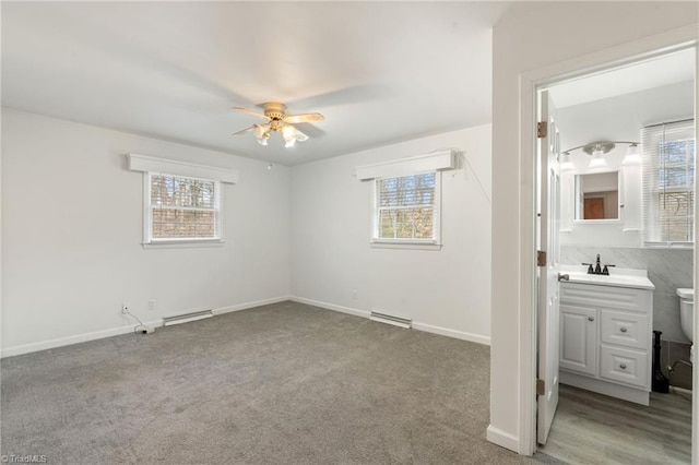 unfurnished bedroom featuring visible vents, baseboard heating, a sink, baseboards, and light colored carpet