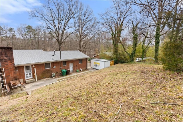 rear view of house featuring brick siding, a lawn, an outdoor structure, and a patio