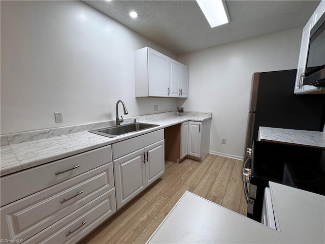 kitchen with a textured ceiling, sink, light hardwood / wood-style flooring, white cabinets, and range