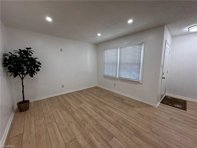 empty room with a textured ceiling and light hardwood / wood-style flooring