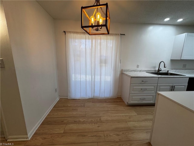 kitchen with sink, hanging light fixtures, a chandelier, light hardwood / wood-style floors, and white cabinets