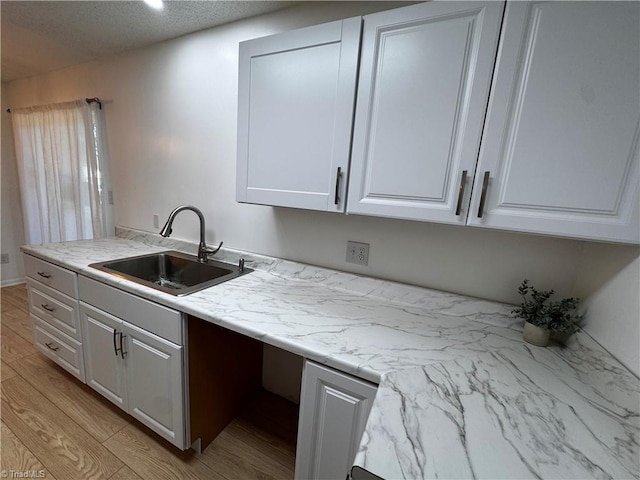 kitchen featuring a textured ceiling, light hardwood / wood-style flooring, white cabinetry, and sink