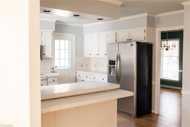 kitchen with crown molding, tile countertops, stainless steel fridge, kitchen peninsula, and white cabinets