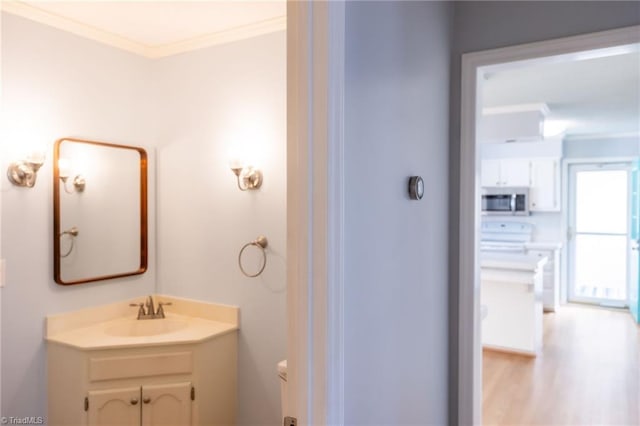 bathroom featuring vanity, wood-type flooring, ornamental molding, and toilet