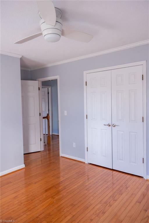 unfurnished bedroom featuring crown molding, ceiling fan, light wood-type flooring, and a closet