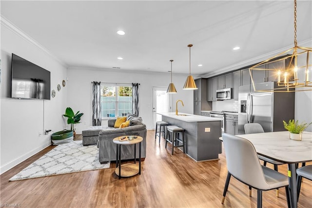 kitchen with ornamental molding, stainless steel appliances, a kitchen island with sink, hanging light fixtures, and a breakfast bar area