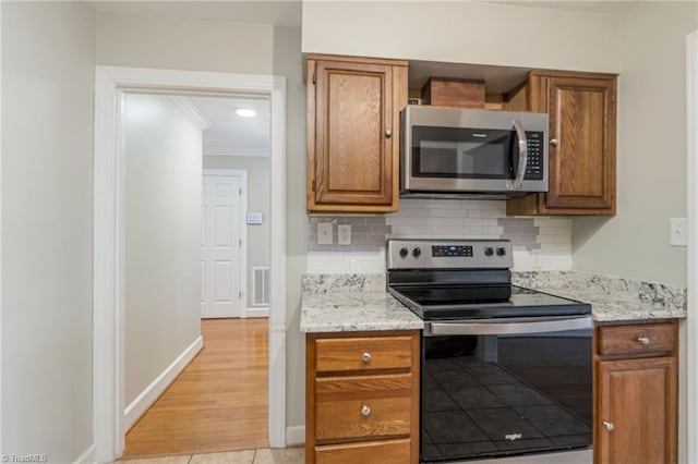 kitchen with backsplash, light stone counters, stainless steel appliances, crown molding, and light tile patterned floors