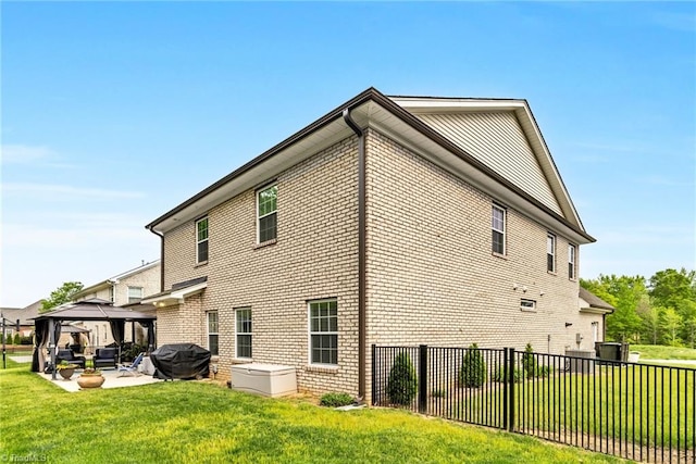 view of side of property with a patio, a lawn, brick siding, a gazebo, and fence