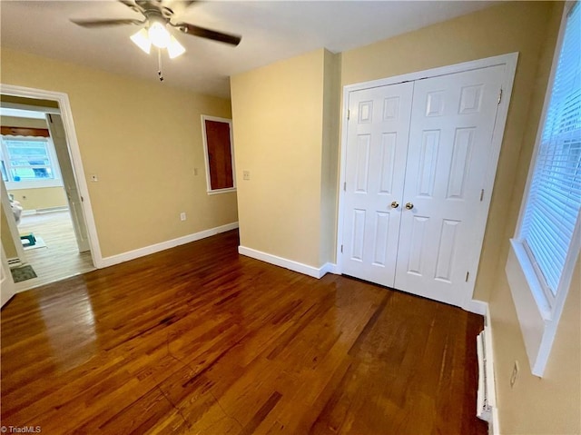 unfurnished bedroom with baseboard heating, ceiling fan, dark hardwood / wood-style flooring, and a closet