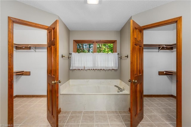 full bath with a garden tub, tile patterned floors, a textured ceiling, a walk in closet, and baseboards