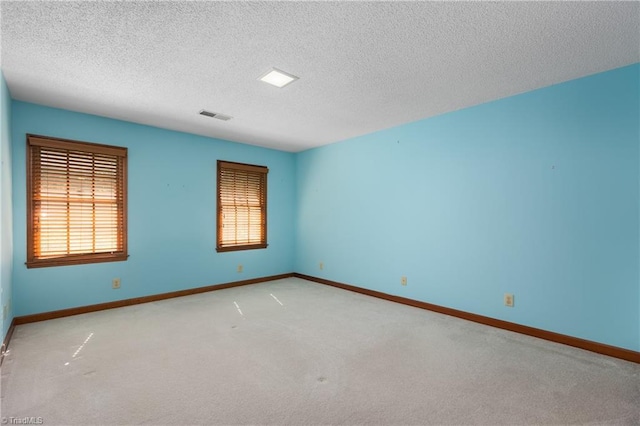 empty room with light colored carpet, baseboards, and a textured ceiling