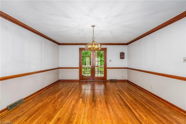 empty room with a chandelier, wood finished floors, baseboards, and ornamental molding