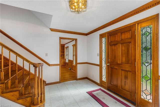 entryway featuring baseboards, stairs, light floors, a textured ceiling, and ornamental molding