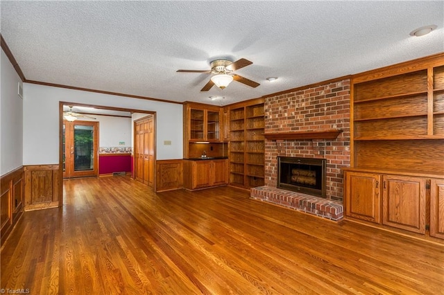 unfurnished living room with a ceiling fan, a textured ceiling, ornamental molding, wainscoting, and wood finished floors