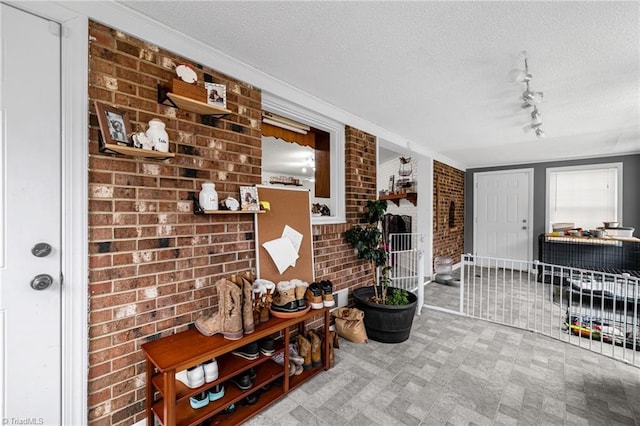 interior space with brick wall, track lighting, and a textured ceiling