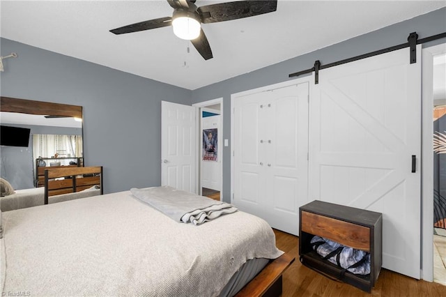 bedroom with dark hardwood / wood-style flooring, a closet, a barn door, and ceiling fan