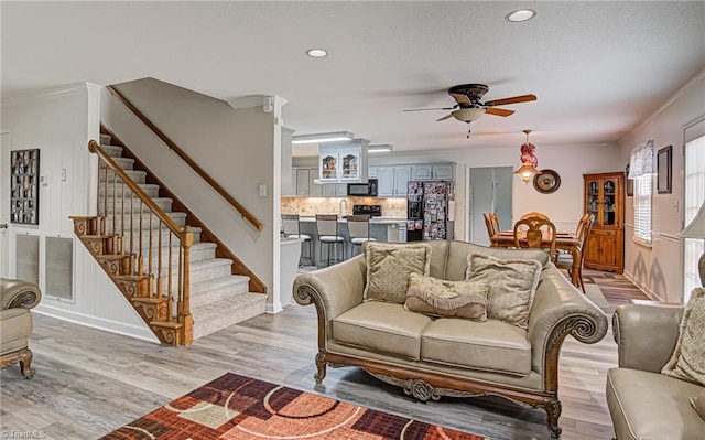 living room featuring ornamental molding, light wood-type flooring, and ceiling fan