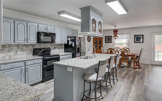 kitchen featuring a center island with sink, light wood-type flooring, black appliances, crown molding, and sink