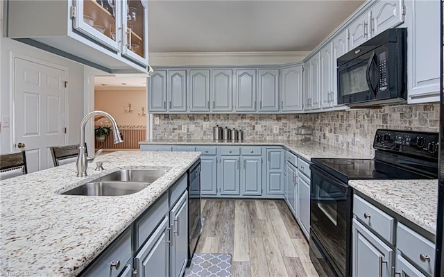 kitchen featuring light stone countertops, black appliances, sink, ornamental molding, and light hardwood / wood-style flooring