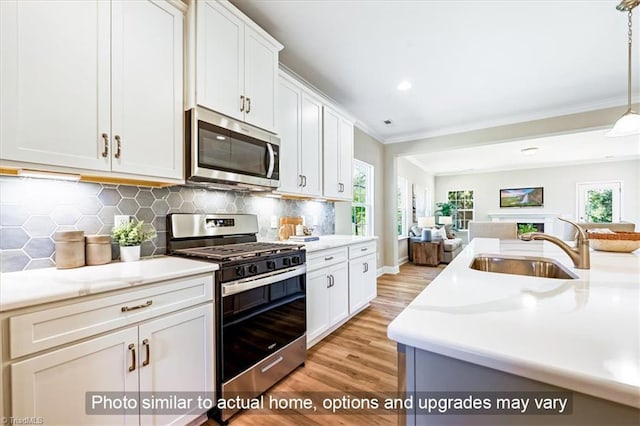 kitchen featuring stainless steel appliances, open floor plan, a sink, light wood finished floors, and crown molding
