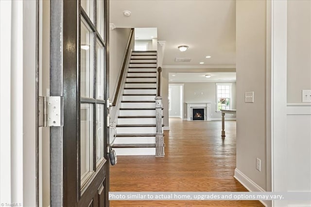 entrance foyer with ornamental molding, baseboards, stairs, wood finished floors, and a warm lit fireplace