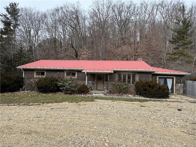 view of front of property featuring a view of trees, stone siding, and metal roof