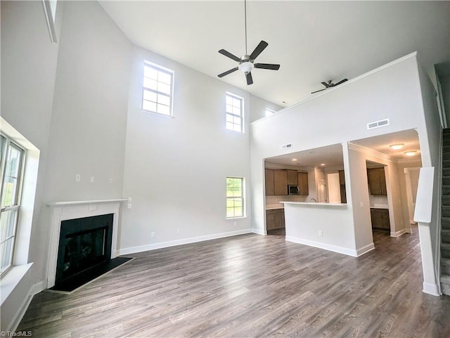 unfurnished living room with a fireplace, ceiling fan, hardwood / wood-style floors, and a towering ceiling