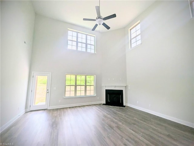 unfurnished living room featuring a premium fireplace, wood-type flooring, ceiling fan, and a towering ceiling