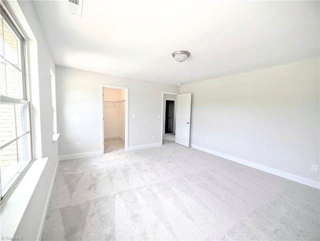 unfurnished bedroom with a closet, light colored carpet, multiple windows, and a spacious closet