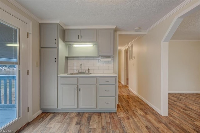 kitchen featuring sink, crown molding, light hardwood / wood-style floors, a textured ceiling, and decorative backsplash