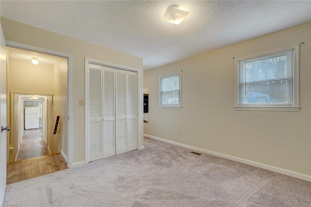 unfurnished bedroom featuring a textured ceiling, white refrigerator, light carpet, and a closet