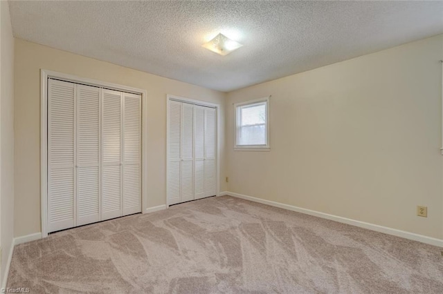 unfurnished bedroom featuring light carpet, a textured ceiling, and two closets