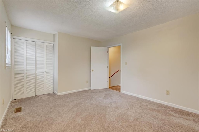 unfurnished bedroom featuring a textured ceiling, light carpet, and a closet