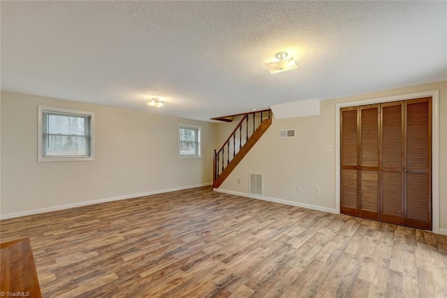 basement with a healthy amount of sunlight, light wood-type flooring, and a textured ceiling