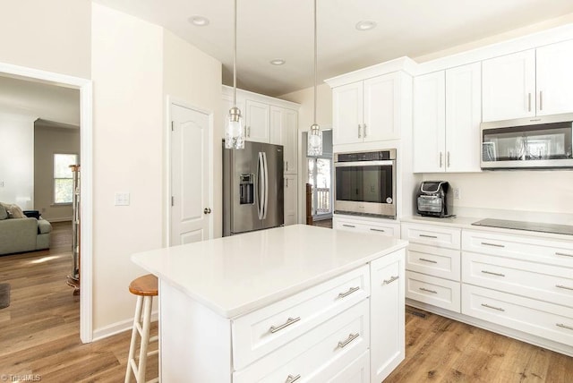 kitchen with white cabinets, a kitchen island, light hardwood / wood-style flooring, stainless steel appliances, and decorative light fixtures