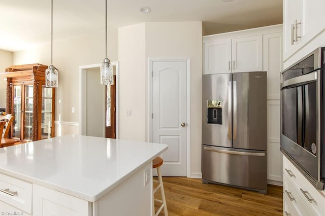 kitchen with a kitchen island, appliances with stainless steel finishes, white cabinetry, wood-type flooring, and decorative light fixtures