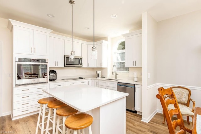 kitchen with white cabinetry, stainless steel appliances, sink, pendant lighting, and a center island