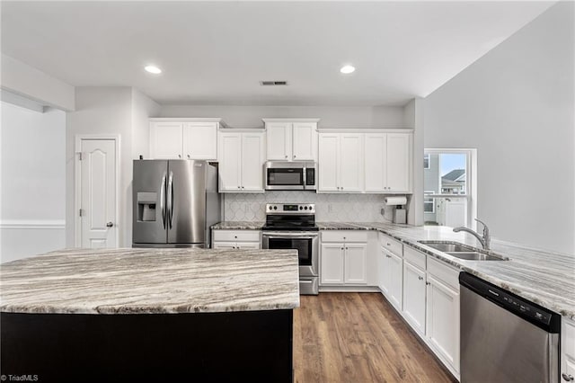 kitchen with sink, appliances with stainless steel finishes, white cabinetry, backsplash, and light stone counters