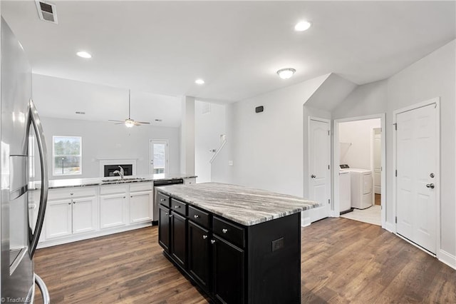 kitchen featuring stainless steel refrigerator, white cabinets, a center island, independent washer and dryer, and light stone countertops