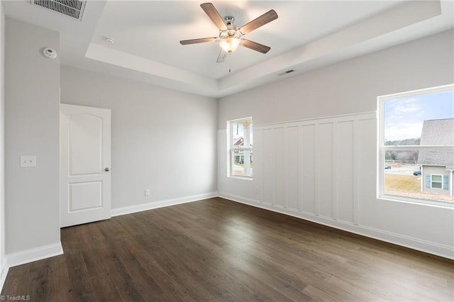 empty room featuring ceiling fan, a tray ceiling, plenty of natural light, and dark wood-type flooring