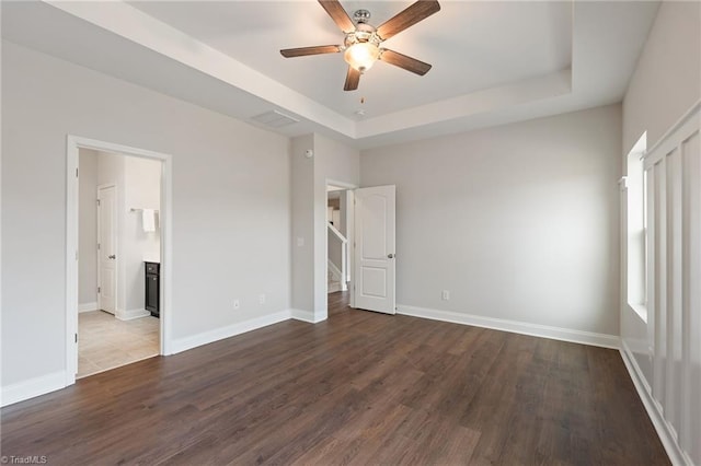 unfurnished bedroom featuring dark hardwood / wood-style floors, connected bathroom, ceiling fan, and a tray ceiling