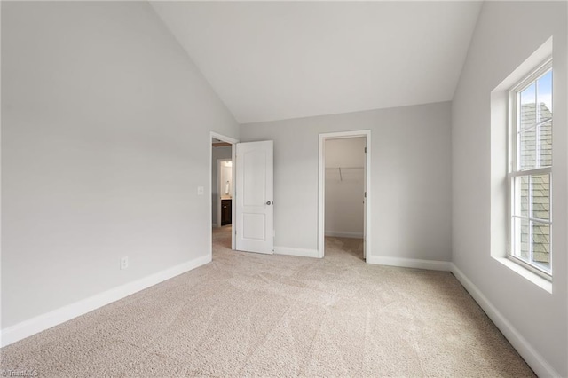 unfurnished bedroom with light carpet, a walk in closet, lofted ceiling, and a closet