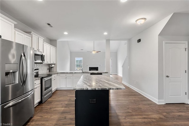 kitchen featuring dark wood-type flooring, appliances with stainless steel finishes, white cabinetry, a center island, and light stone countertops