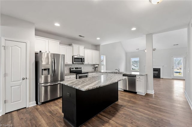 kitchen with white cabinetry, stainless steel appliances, a center island, light stone countertops, and kitchen peninsula