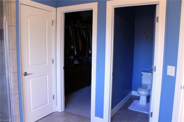 full bathroom featuring a spacious closet, tile patterned flooring, toilet, and baseboards