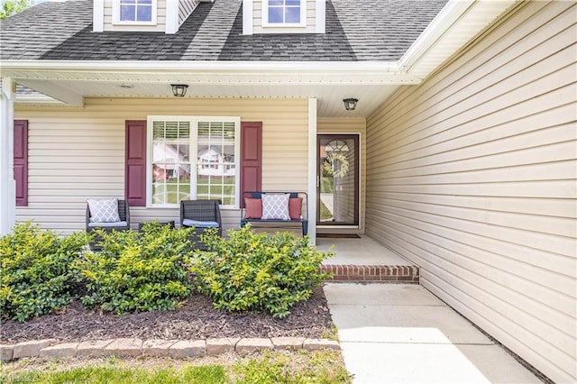 view of exterior entry with a shingled roof and covered porch